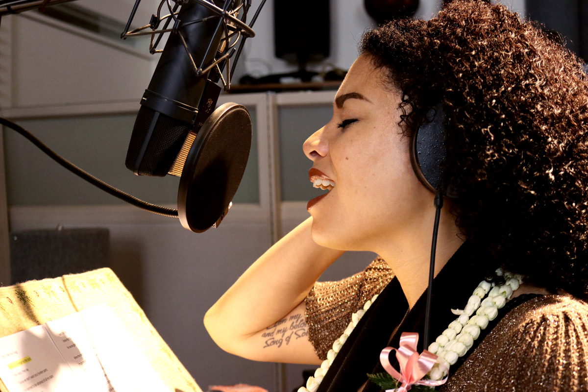 Jenene Ahia singing into a microphone in a recording studio