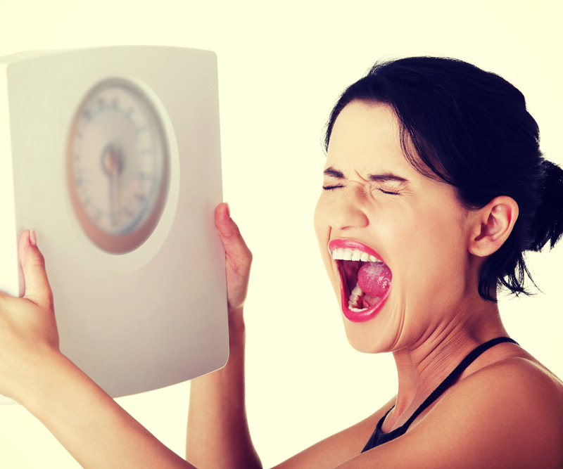 young woman holding up scale and screaming in frustration