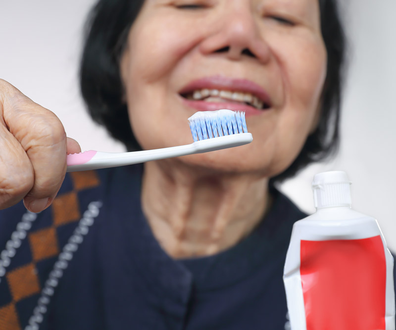 close-up of an elderly Asian woman squeezing toothpaste onto a toothbrush