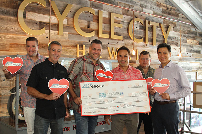 Group of men holding red hearts and a ceremonial check to Kapiolani for $20,000