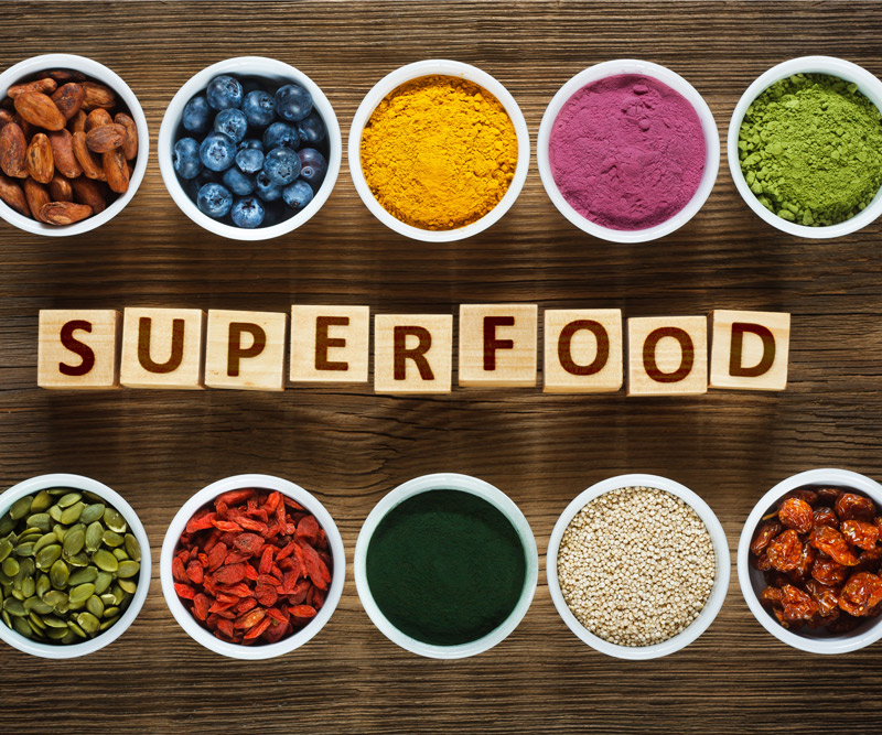 the word Superfoods spelled out in blocks surrounded by measuring cups of popular superfoods and supplements
