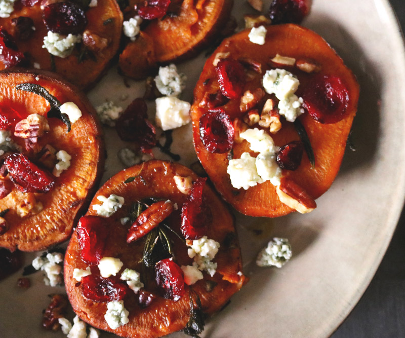 a plate of sliced sweet potato rounds topped with crumbled blue cheese, chopped pecans and dried cranberries