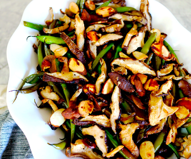 a white serving plate of Garlicky Green Beans topped with crispy mushrooms and almonds