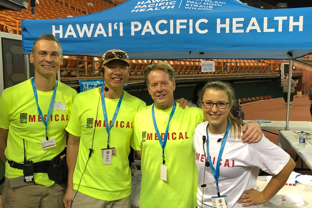 three men in neon green volunteer shirts and a woman in a white volunteer shirt stand in front of a blue pop-up tent that says Hawaii Pacific Health