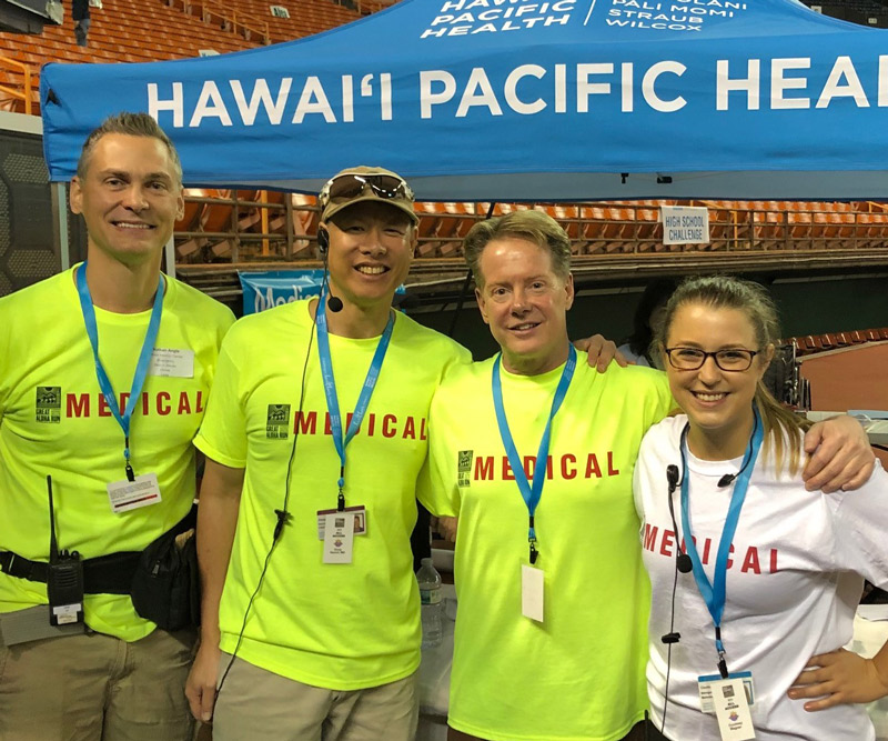 three men in neon green volunteer shirts and a woman in a white volunteer shirt stand in front of a blue pop-up tent that says Hawaii Pacific Health
