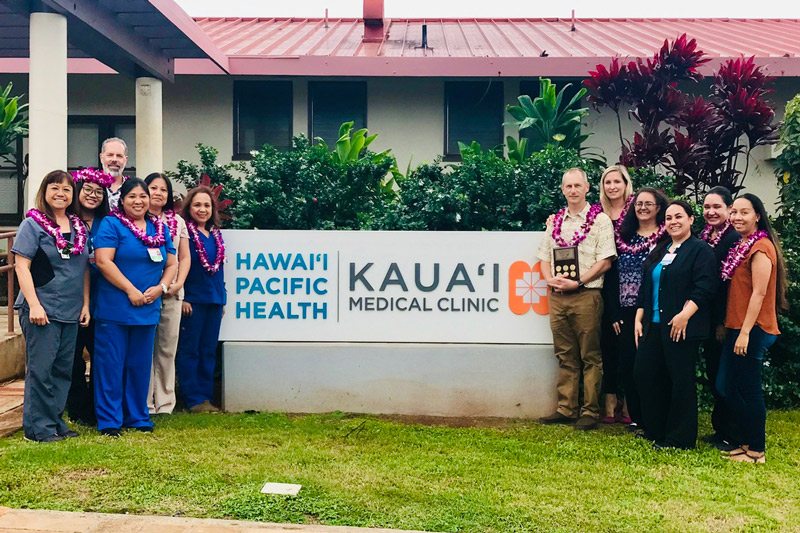 group of people wearing lei and holding an award stand in front of Kauai Medical Clinic sign