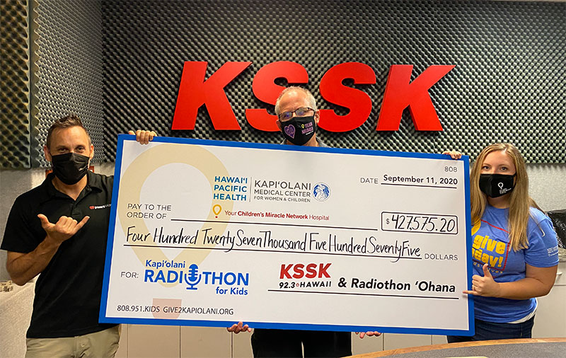Three people holding a ceremonial check in front of KSSK radio sign
