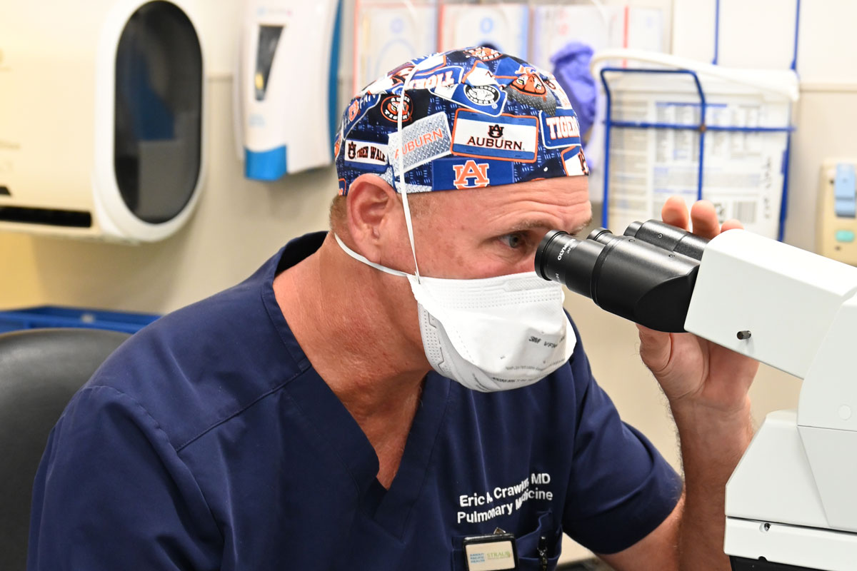 a doctor in scrubs looks into a microscope
