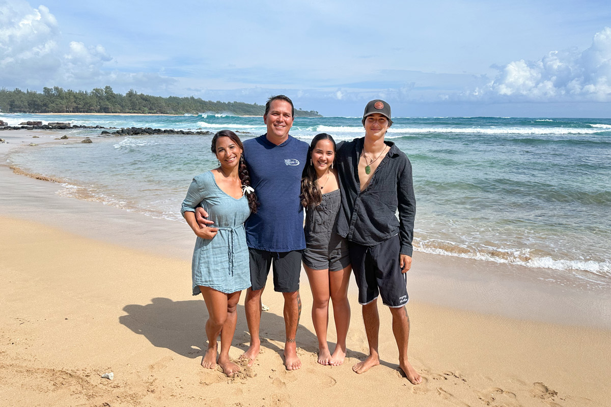 A woman and man stand with their teenage daughter and teenage son on the shore of Hanalei Bay on Kauai.