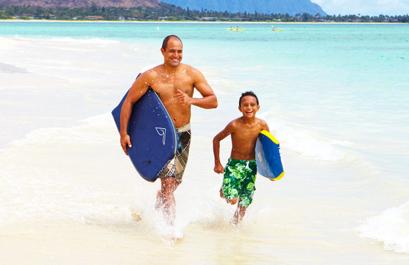 father and son with boogie boards running on the beach