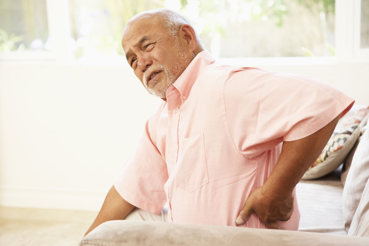 an older man sitting in a chair touching his lower back