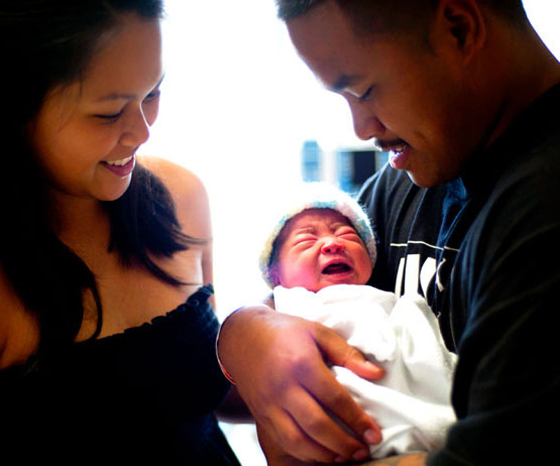 newborn baby in the arms of dad with mom smiling