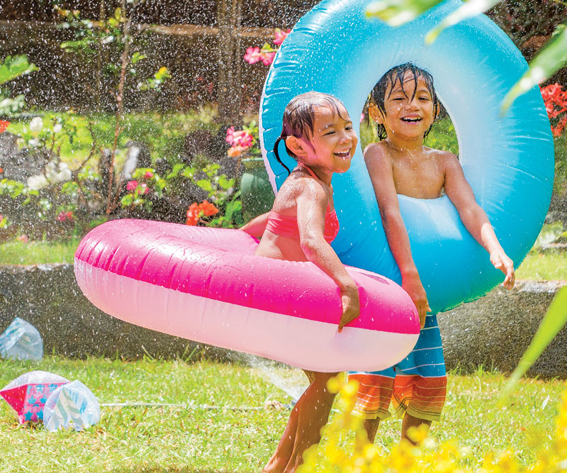 two kids playing in the yard with a sprinkler and blow up pool toys