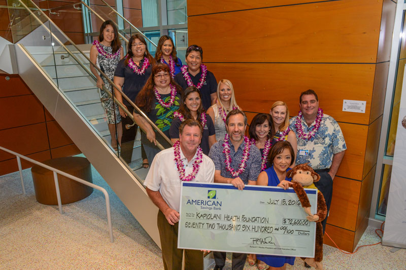 American Savings Bank employees standing on stairs holding up a large donation check