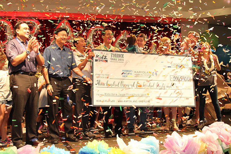 a group celebrating on stage with a large check with confetti falling down