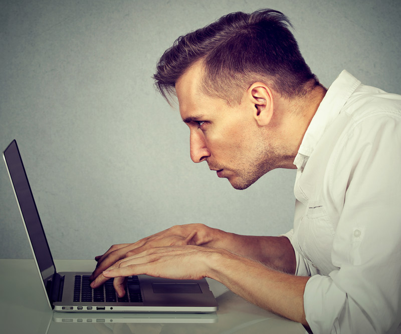 man crouched uncomfortably in front of his laptop