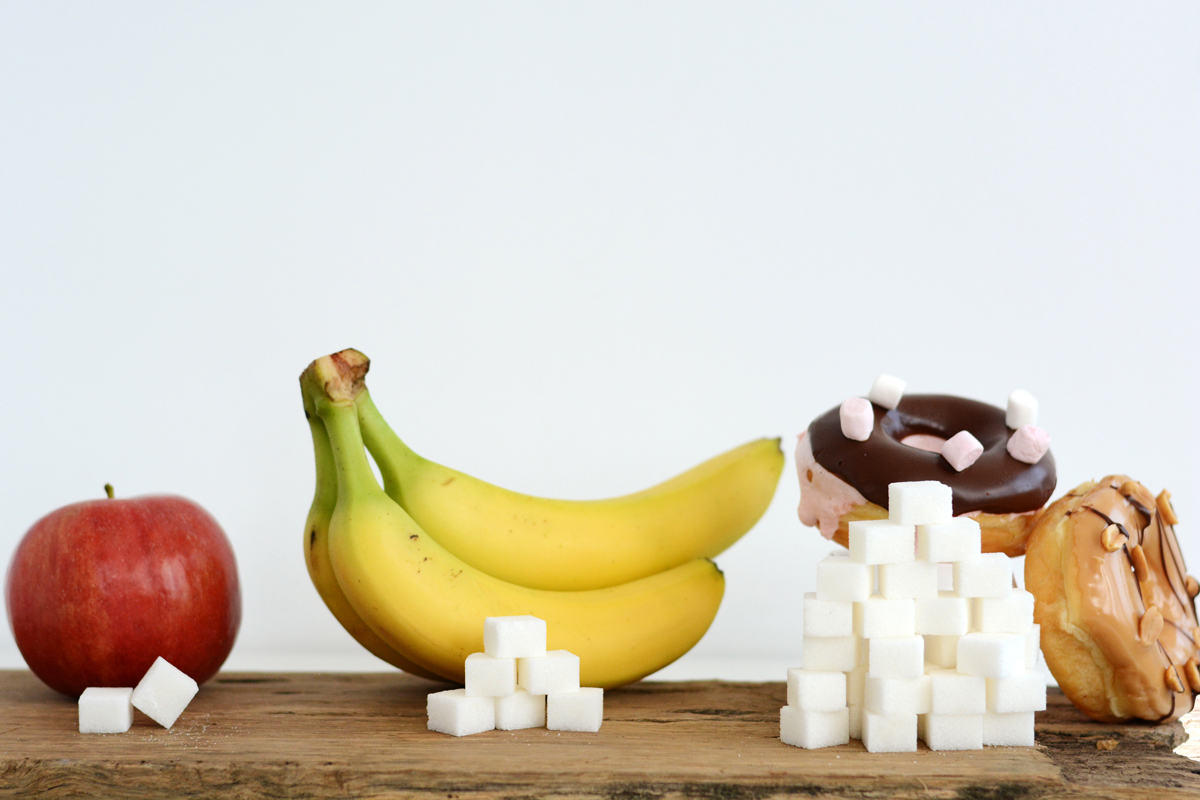 A photo shows an apple, banana and donuts with sugar cubes to depict how much sugar is found in each food item.