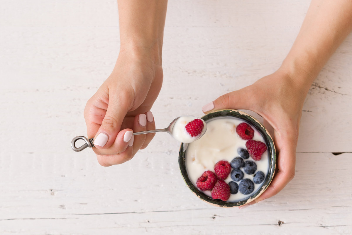 Woman's hands holding a spoon in one hand and a bowl of yogurt and fruit in the other