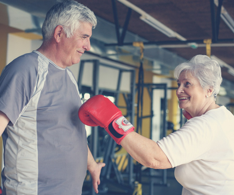 An older women playfully spars with her husband in a gym