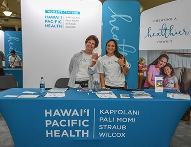 Two women standing behind the Women's Center Booth at the Great Aloha Run Expo