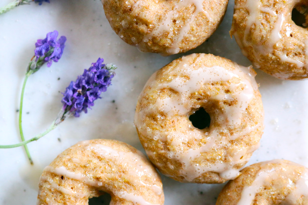 A batch of Baked Lavender & Rose Donuts are displayed on a counter top with fresh sprigs of lavender next to them