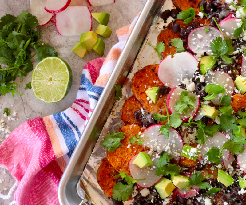 a sheet pan of Loaded Sheet Pan Sweet Potato Nachos sits on a brightly colored hand towel on a kitchen counter