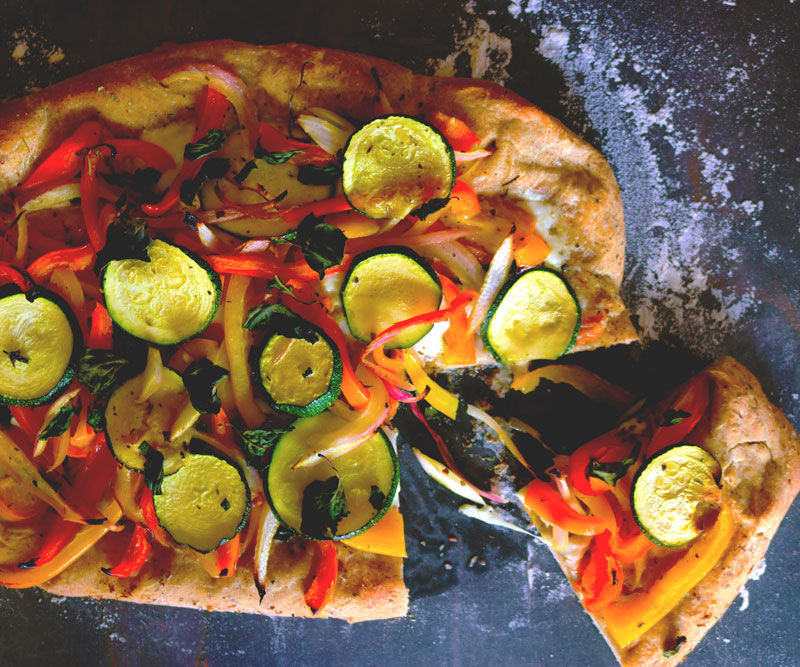 Freshly made Pizza with Peppers & Zucchini on a counter top generously dusted with flour