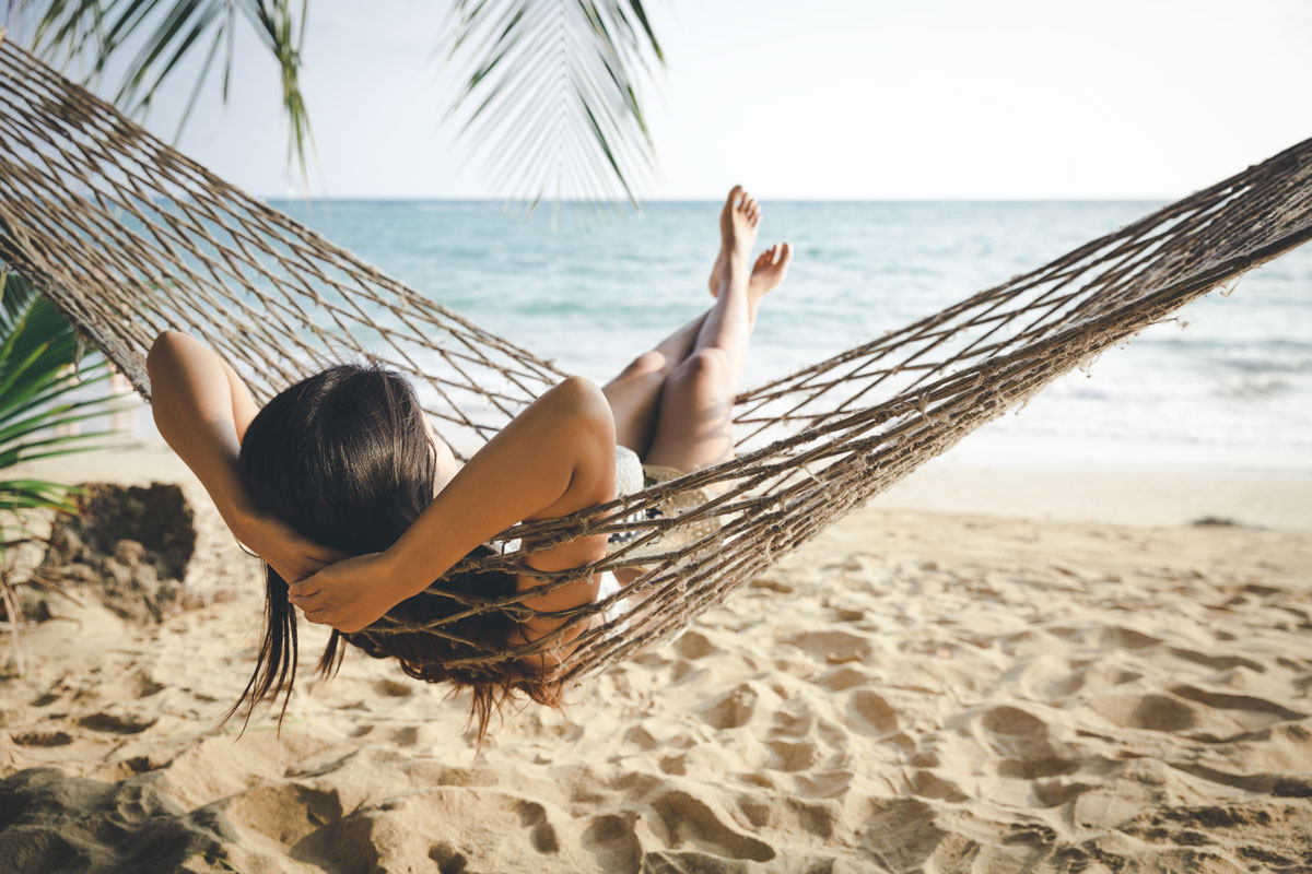 a woman relaxes in a hammock by the beach