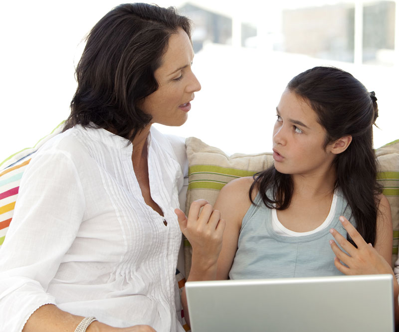 a teenage girl talks with her mother about a website on a computer
