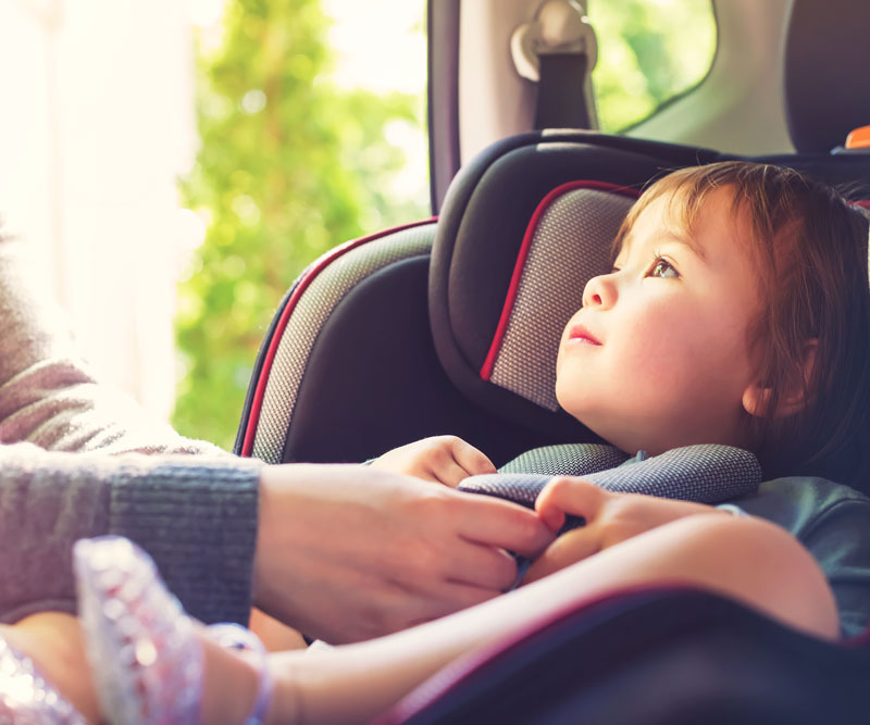 young child getting buckled into a car safety seat