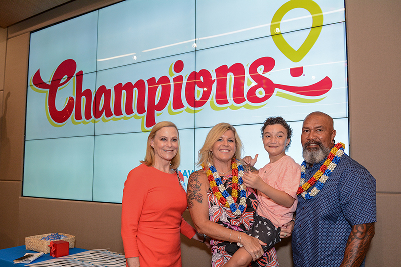 Two women, child and man in front of screen with Children's Miracle Network Hospitals Champions logo