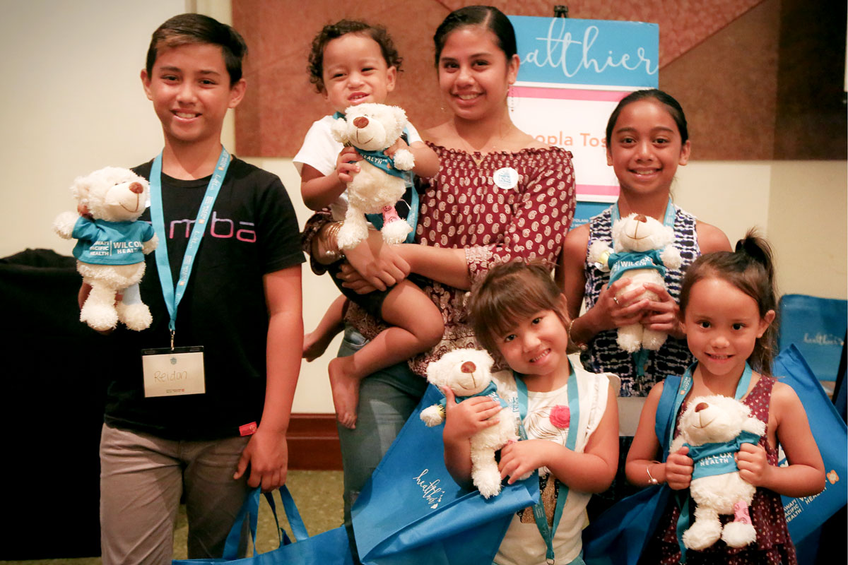 a mother and her five children smile while holding teddy bears and Kids Summer Fest tote bags