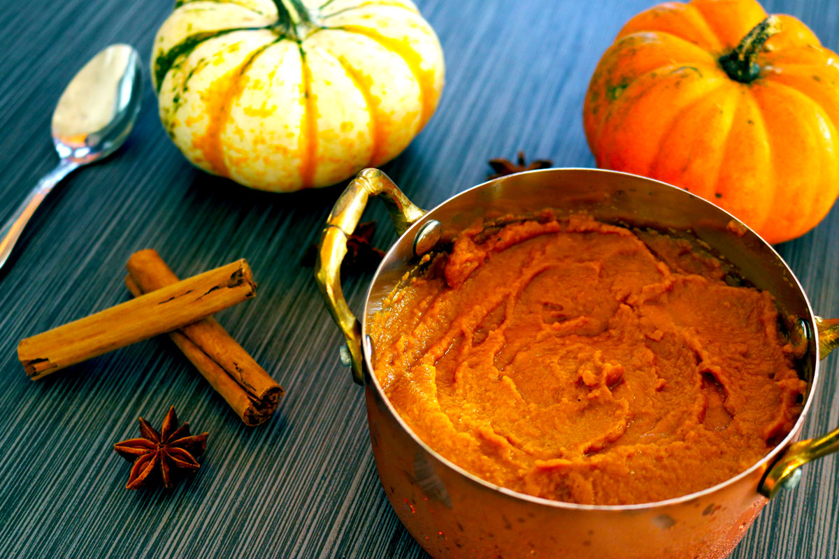 a bowl of Pumpkin Pudding sits on a table decorated with pumpkins, cinnamon sticks and star anise seeds