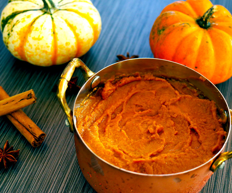 a bowl of Pumpkin Pudding sits on a table decorated with pumpkins, cinnamon sticks and star anise seeds