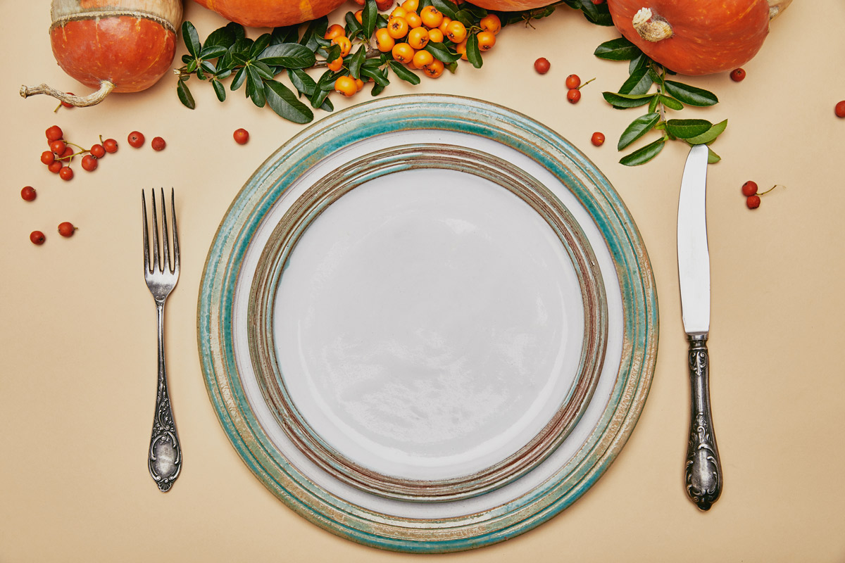 top view of thanksgiving table set with a plate, fork and knife and decorated with pumpkins and cranberries