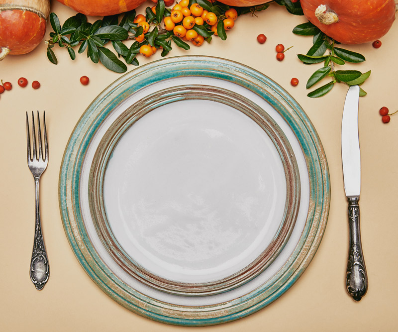 top view of thanksgiving table set with a plate, fork and knife and decorated with pumpkins and cranberries