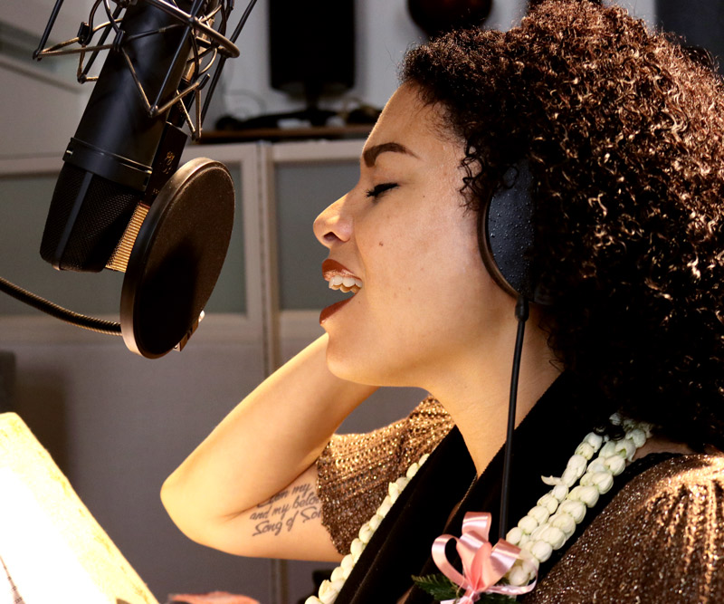 Jenene Ahia singing into a microphone in a recording studio