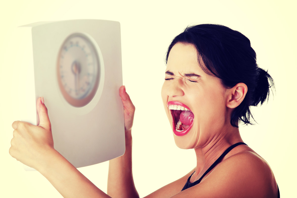 young woman holding up scale and screaming in frustration