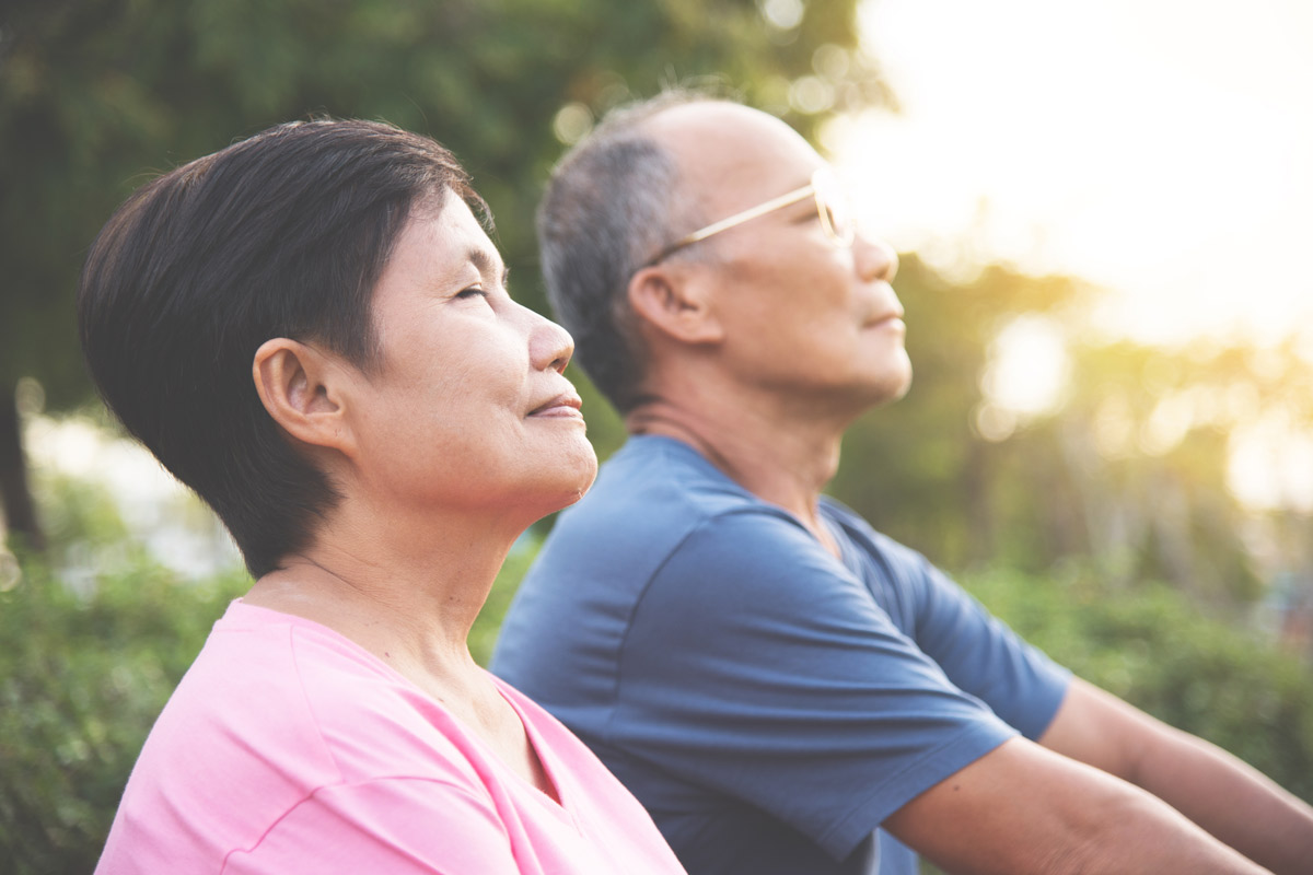 an elderly couple practices meditative breathing exercises in an outdoor park