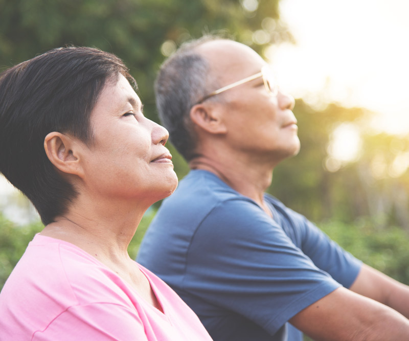 an elderly couple practices meditative breathing exercises in an outdoor park