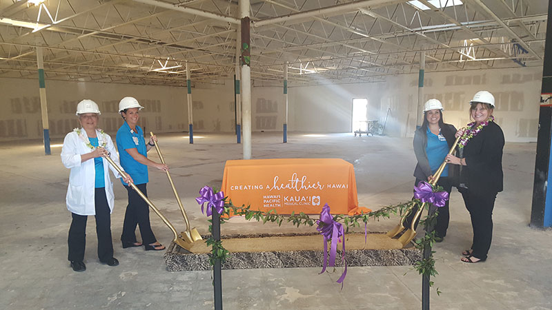 Four women wearing construction hats and holding shovels for groundbreaking ceremony