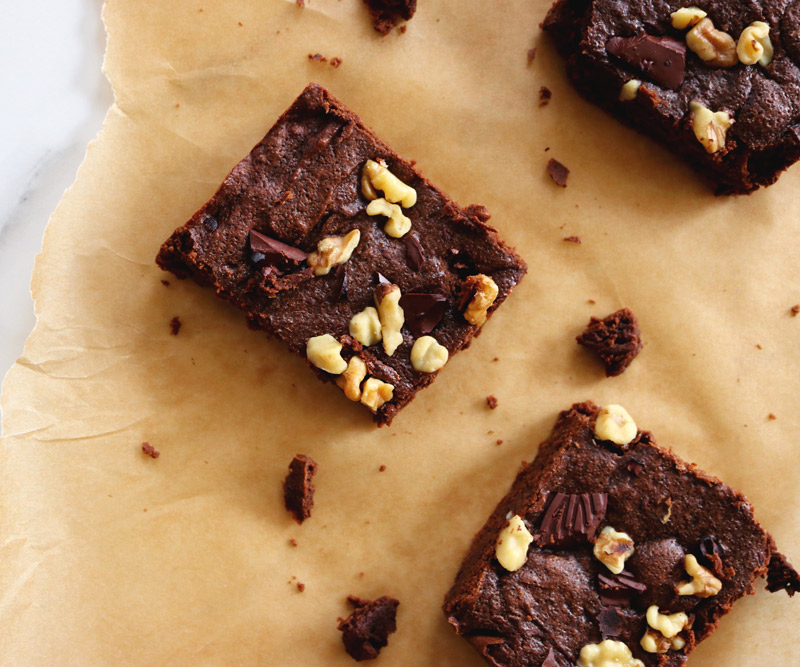 Three Fudgy Keto Brownies arranged on a torn sheet of parchment paper rest on a marble counter top