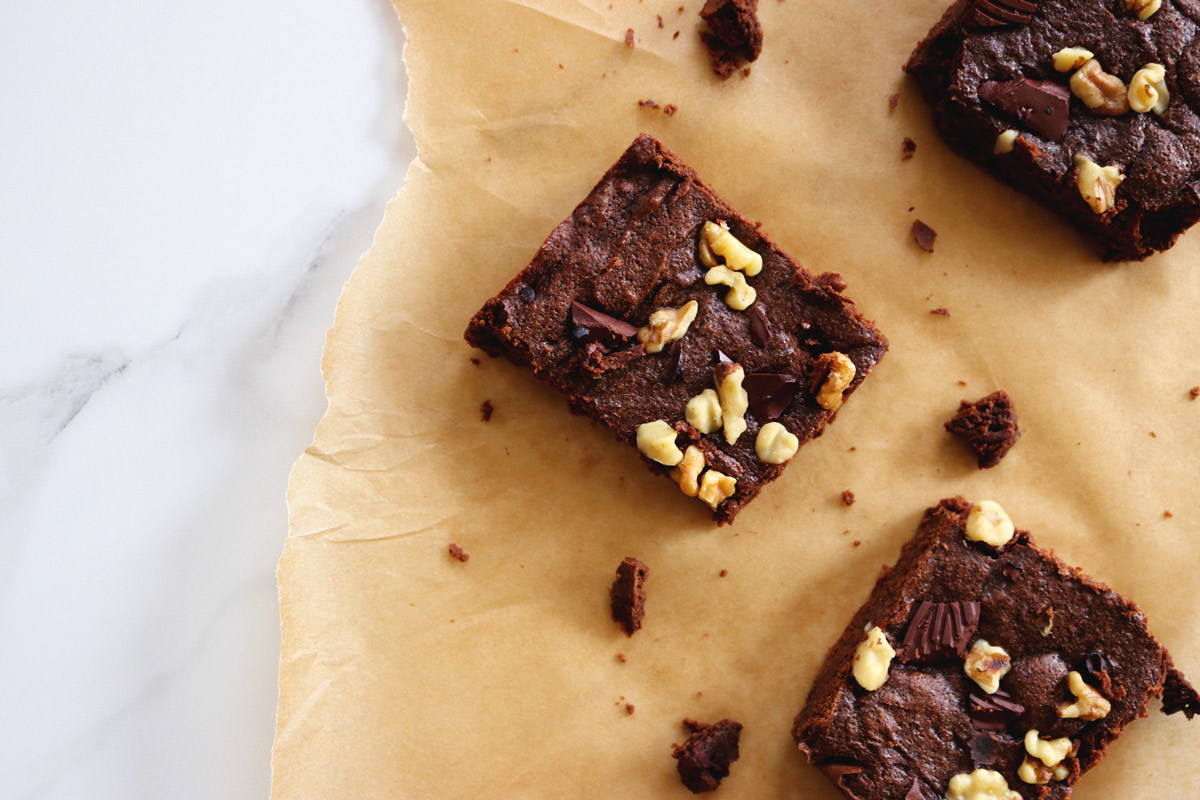 Three Fudgy Keto Brownies arranged on a torn sheet of parchment paper rest on a marble counter top