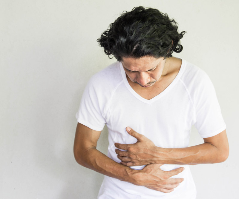 middle-aged man in a white T-shirt holds his stomach with a look of pain on his face to indicate possible colon cancer