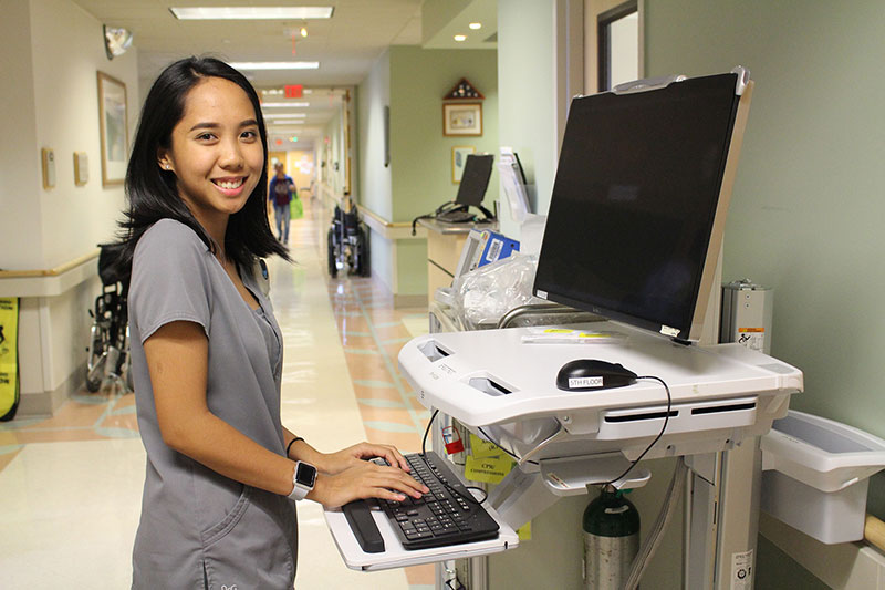 Girl in medical scrubs in hospital hallway on computer