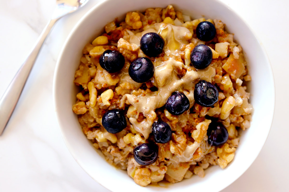 a bowl of Cauli-Oats topped with blueberries sits on a marble counter top with a spoon resting in the background