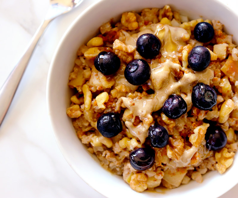 a bowl of Cauli-Oats topped with blueberries sits on a marble counter top with a spoon resting in the background