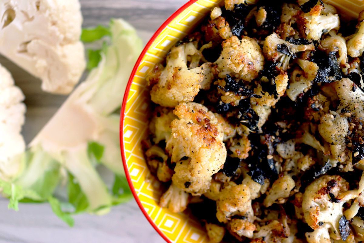 a closeup of a bowl of Cauliflower Hurricane Popcorn on a counter top with cauliflower florets next to it