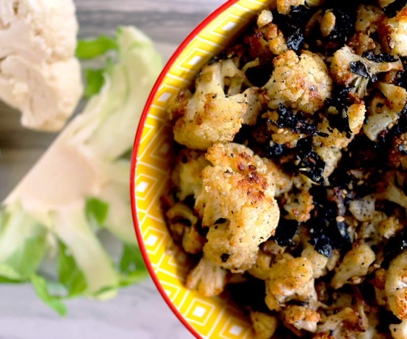 a closeup of a bowl of Cauliflower Hurricane Popcorn on a counter top with cauliflower florets next to it