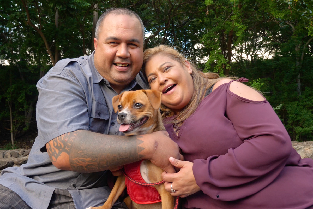 Charlyn Esera and fiance Chad sit together hugging with their small brown dog, Honey Girl, between them